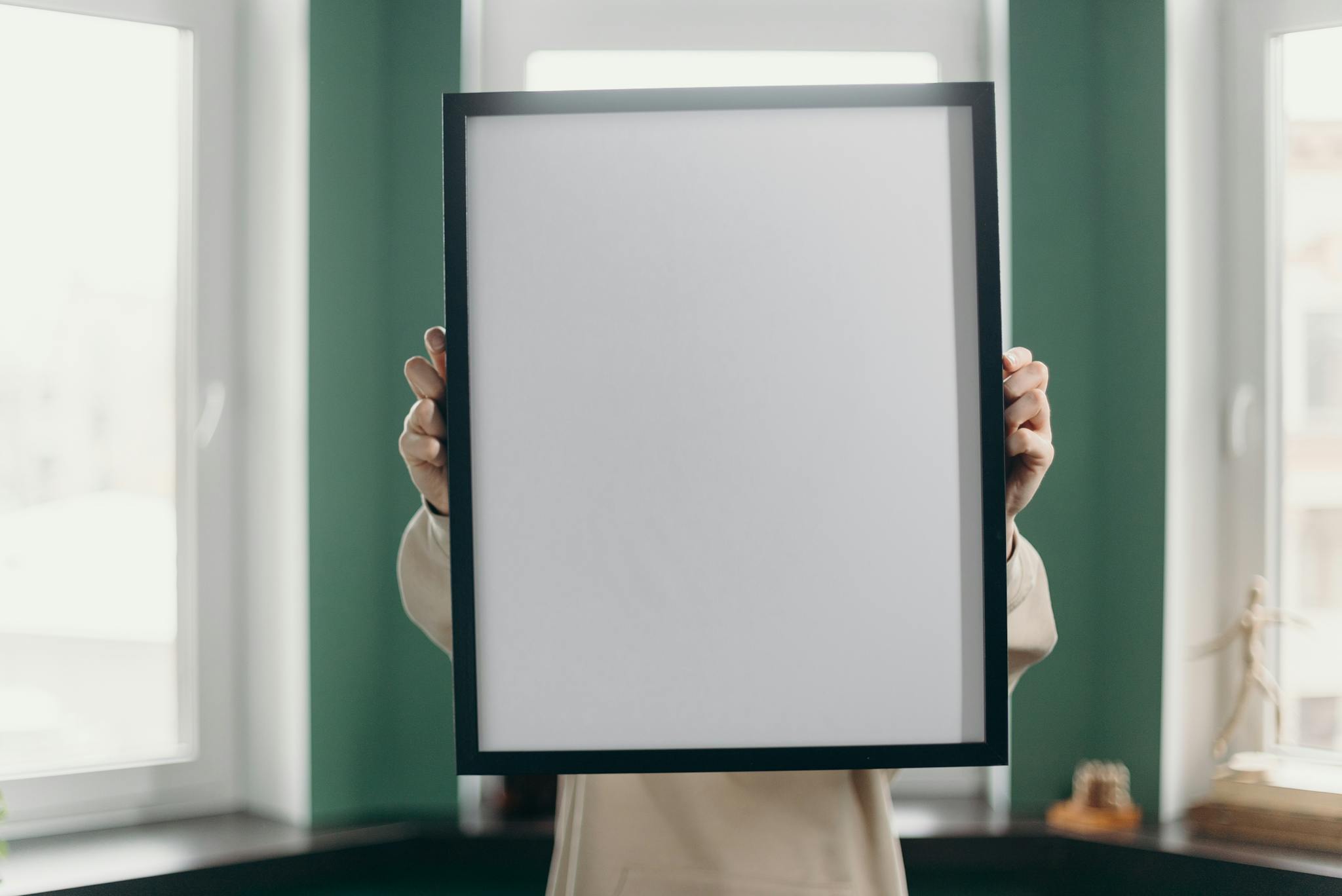 Adult holding a blank photo frame in an indoor, minimalist setting. Ideal for mockups and design.